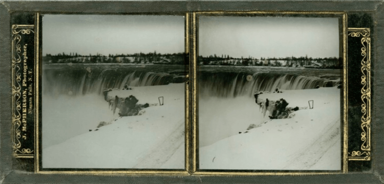 Two nearly identical black and white photographs side by side in a glass frame. The photos show Niagara Falls in winter. The landscape is covered in snow and ice.